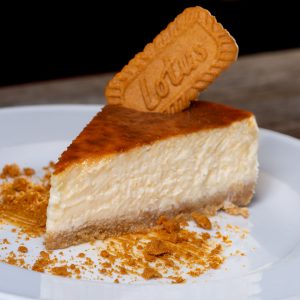 Creamy cheesecake topped with a Lotus biscuit, served on a white plate.